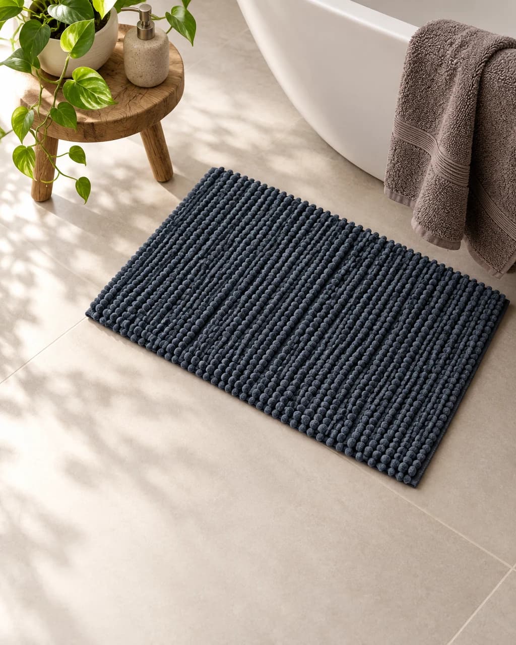 Brown towel over a white bathtub and a charcoal pompom bath mat on a tiled bathroom floor